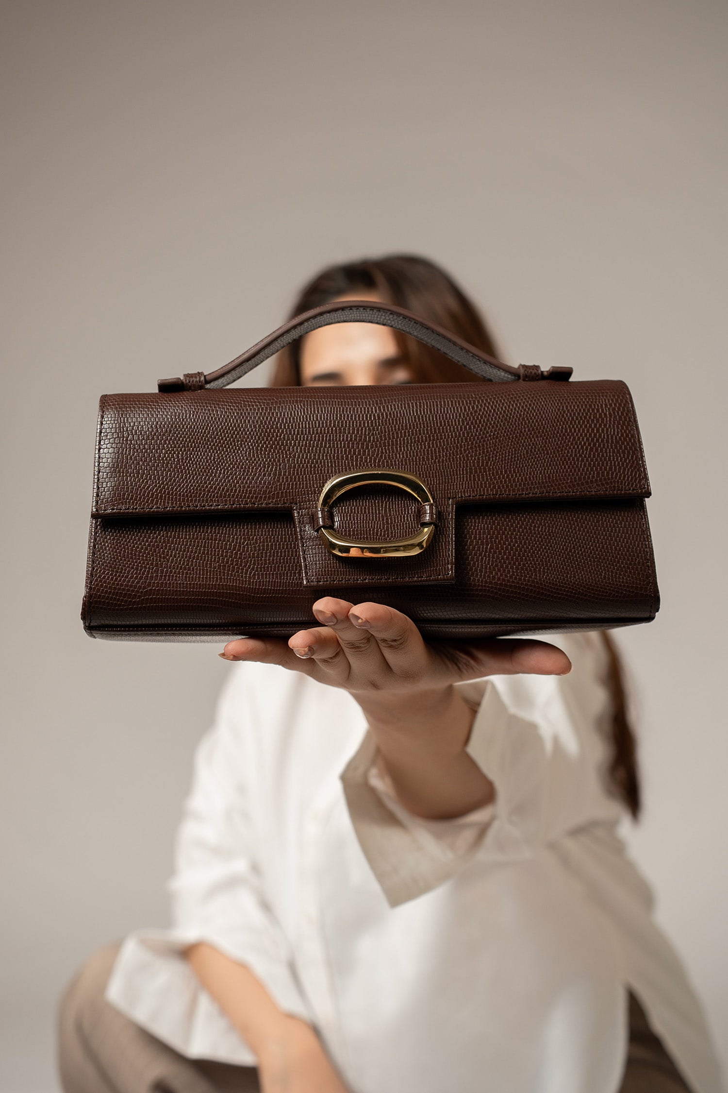 Womens leather top handle shoulder bag in dark brown colour with reptile texture and oval gold buckle by JULKE.