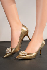 Women's high heel pointed toe pumps in dark gold colour with shiny reptile texture and flower shaped white rhinestone brooch by JULKE