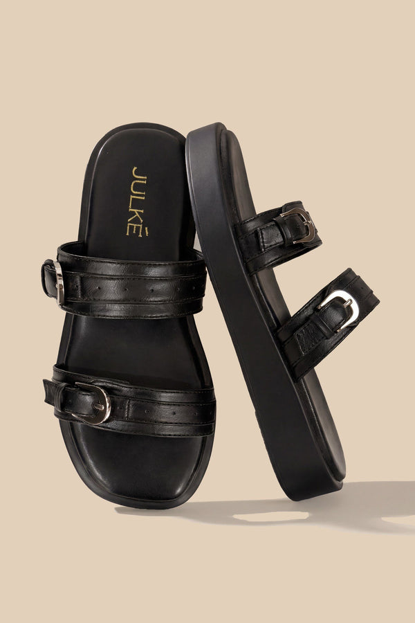 A pair of black double-strap platform slide sandals with silver-tone buckles, shown on a solid beige background. The brand name 'JULKE' is printed in gold on the insole of the left sandal.