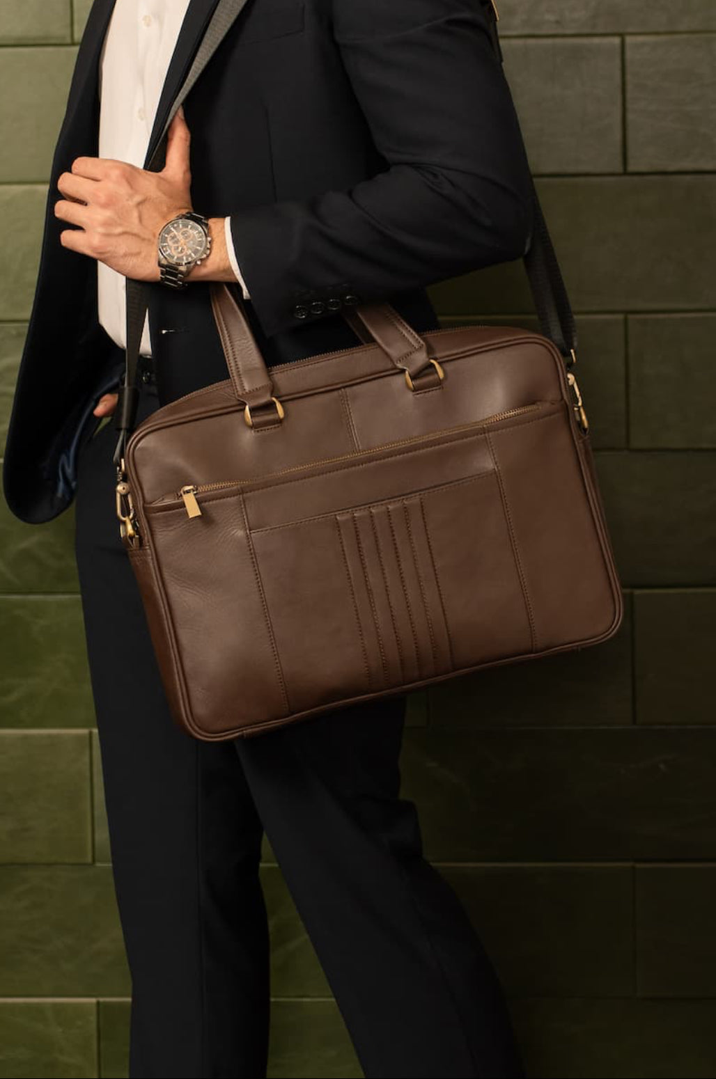 Man holding a brown leather briefcase against a green tiled wall