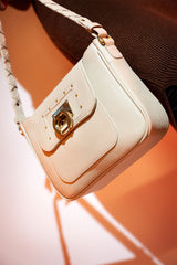 Women's grain texture leather shoulder bag in off white colour with woven shoulder strap and metallic gold doorknocker style buckle by JULKE. 