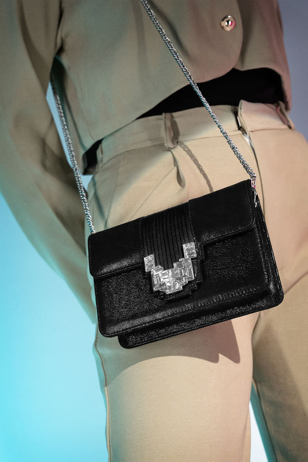 Women's suede leather clutch bag in shiny black colour with satin pleated flap and geometric transparent rhinestone brooch by JULKE.