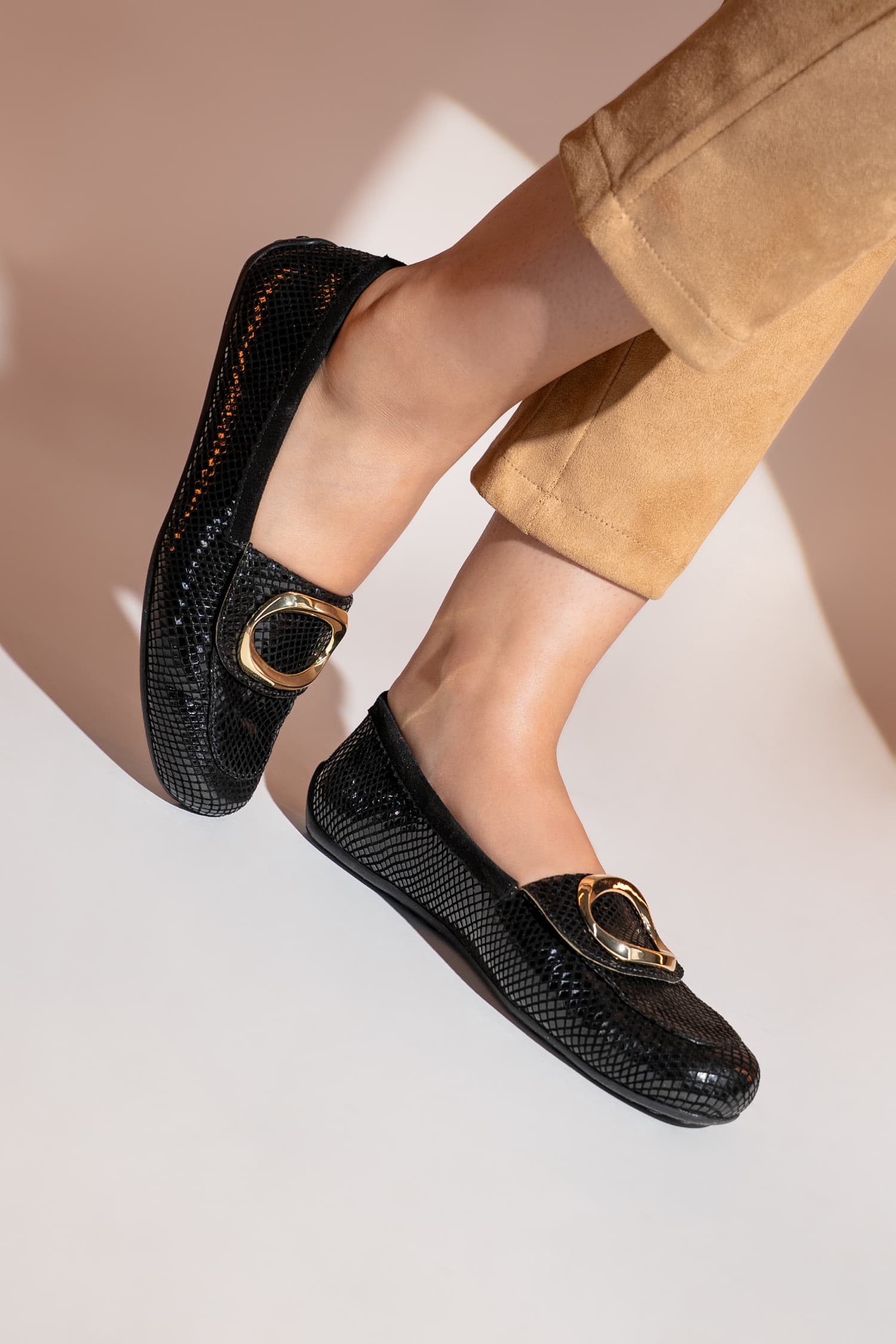 Black loafers with gold buckles worn by a person on a neutral background