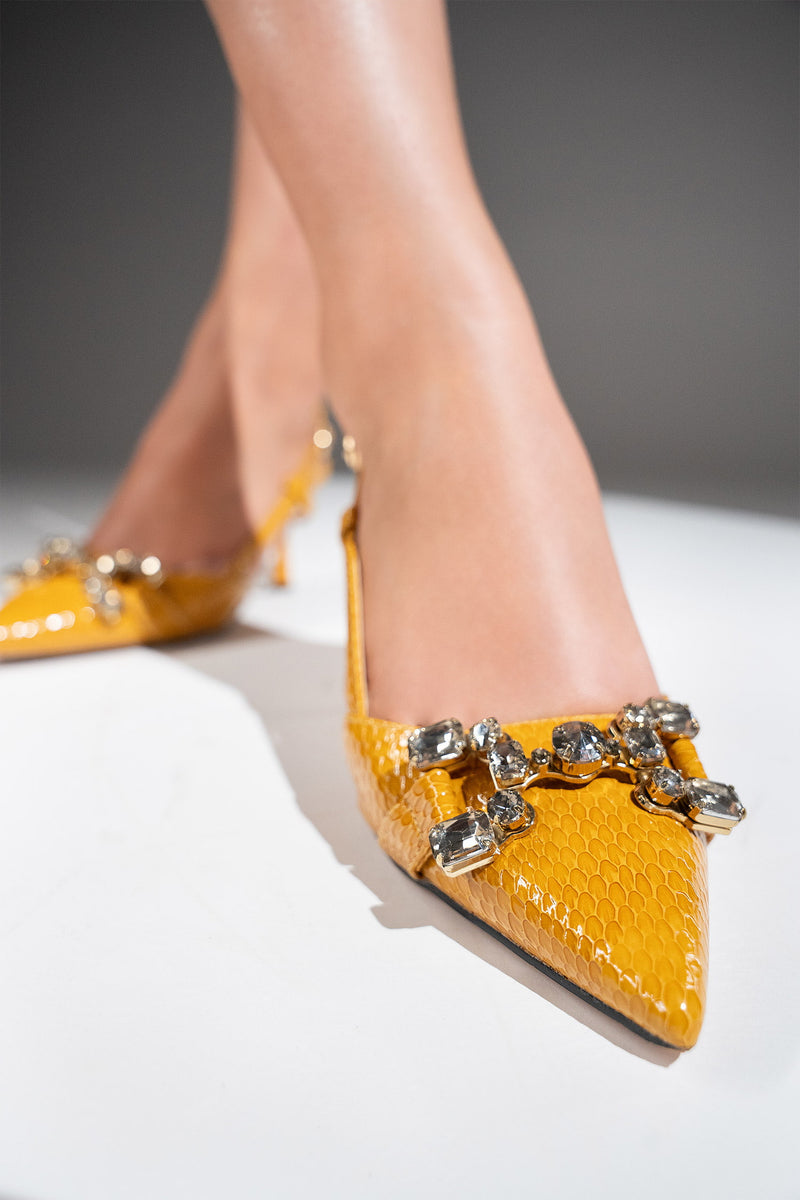 Women's sling back pointed toe heels in mustard yellow colour with glossy dragon scale texture and rhinestone horse-bit buckle by JULKE. 