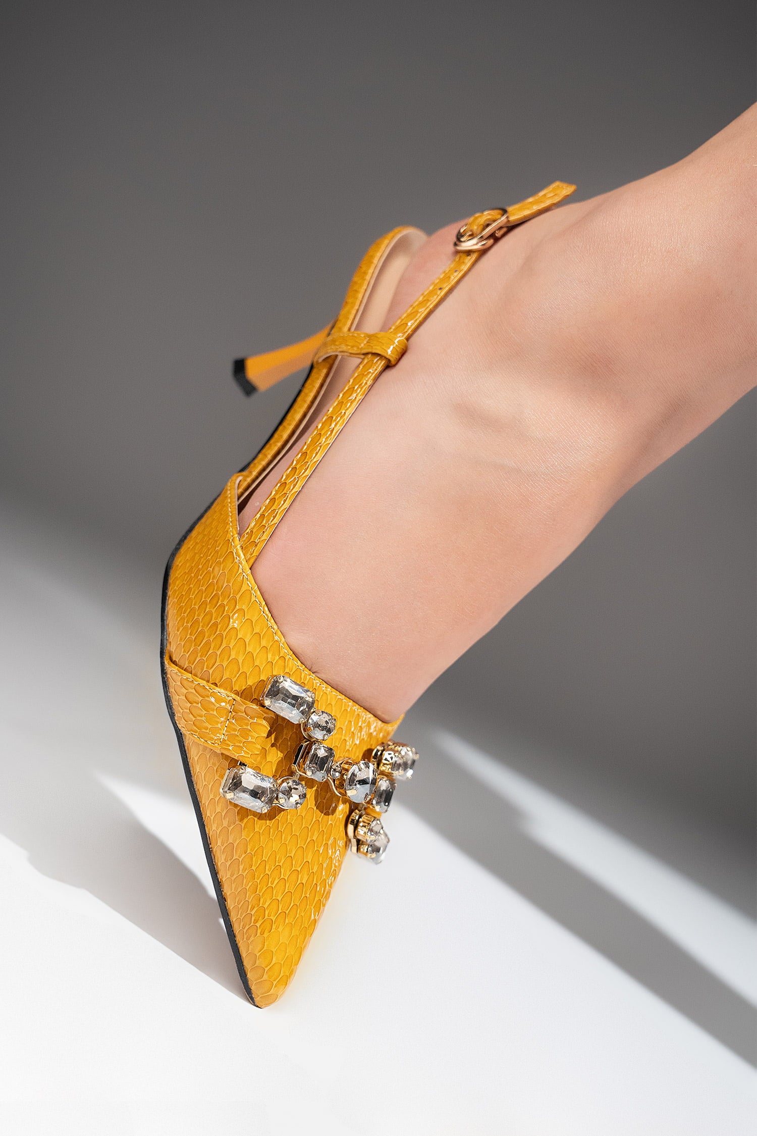 Women's sling back pointed toe heels in mustard yellow colour with glossy dragon scale texture and rhinestone horse-bit buckle by JULKE. 