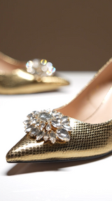 Women's high heel pointed toe pumps and matching leather hand bag in dark gold colour with shiny reptile texture and flower shaped white rhinestone brooch with by JULKE